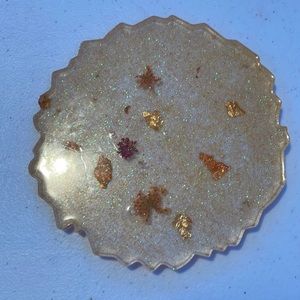 Homemade resin coaster with orange glitter, gold flakes, and flowers.